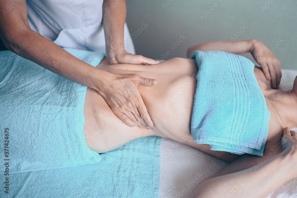 Young unrecognizable woman lying on massage table and enjoying therapeutic massage. Body care, losing weight concept. Hands masseur massage therapist doing anti-cellulite massage in spa clinic.
