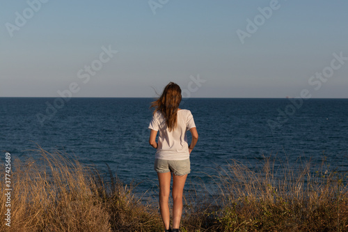 Mujer paseando por una pradera en la que se divisa el mar en el fondo