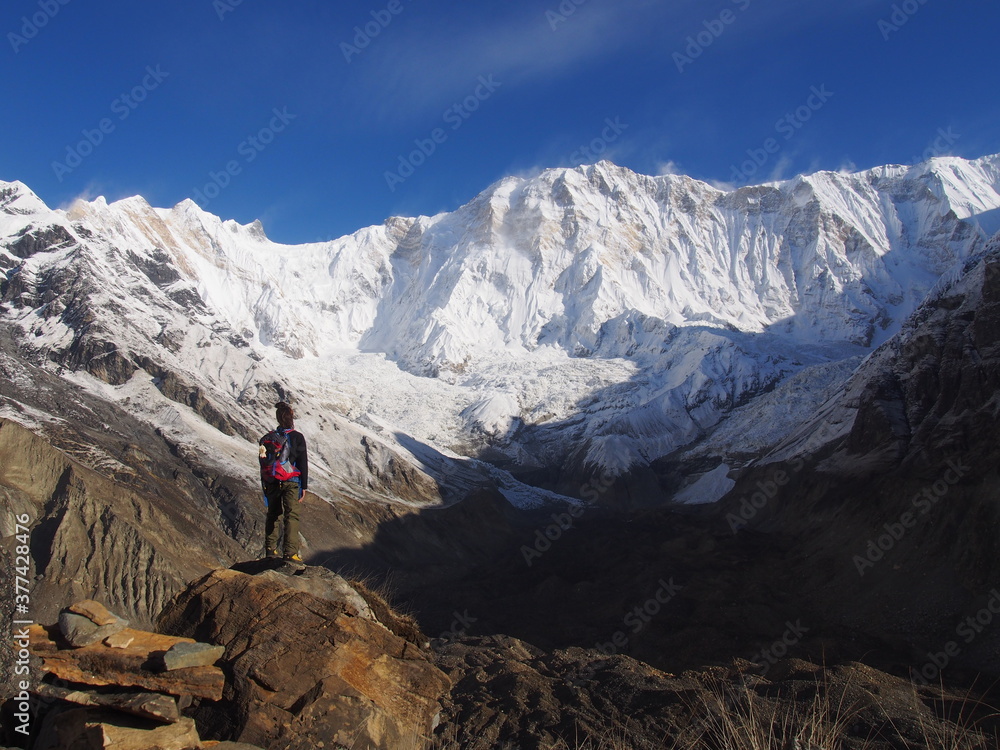 A mountain climber standing in front of a snow-covered Himalayas in the blue skies, ABC (Annapurna Base Camp) Trek, Annapurna, Nepal