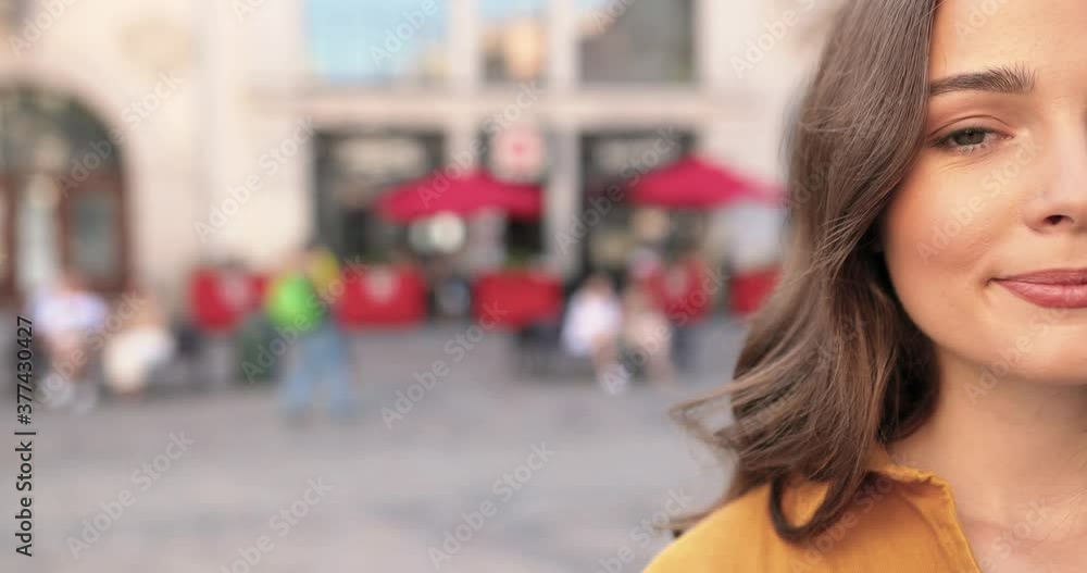 Portrait of Caucasian beautiful young woman looking at camera and smiling cheerfully. Female beauty concept. Outside in city square. Close up of half face of pretty girl with joyful happy smile. Portrait of Caucasian beautiful young woman looking at camera and smiling cheerfully. Female beauty concept. Outside in city square. Close up of half face of pretty girl with joyful happy smile.