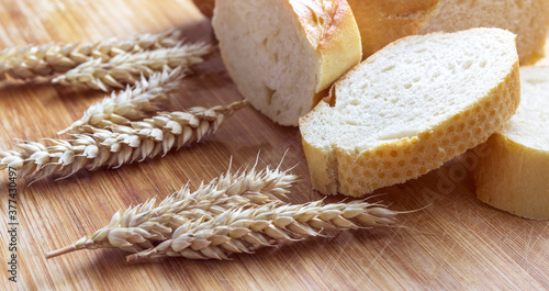 Sliced bread on a wooden board, with wheat spikelets.