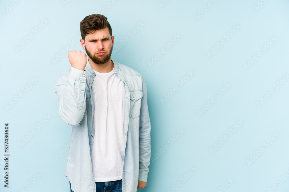Young caucasian man isolated on blue background showing fist to camera, aggressive facial expression. Young caucasian man isolated on blue background showing fist to camera, aggressive facial expression.