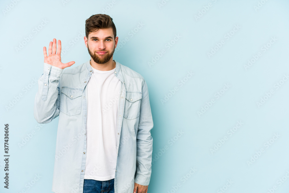 Young caucasian man isolated on blue background smiling cheerful showing number five with fingers. Young caucasian man isolated on blue background smiling cheerful showing number five with fingers.