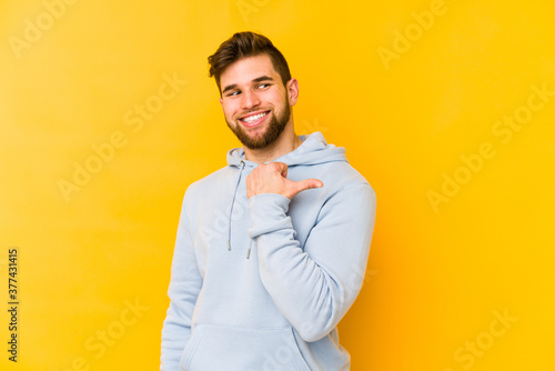 Young caucasian man isolated on yellow background points with thumb finger away  laughing and carefree.