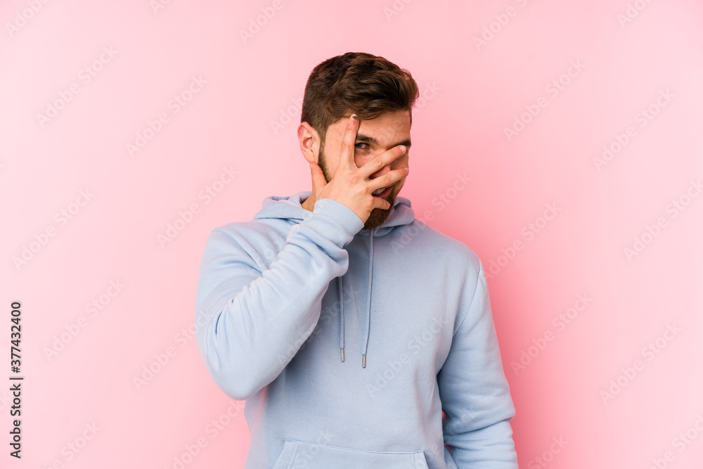 Young caucasian man isolated on pink background blink at the camera through fingers, embarrassed covering face. Young caucasian man isolated on pink background blink at the camera through fingers, embarrassed covering face.