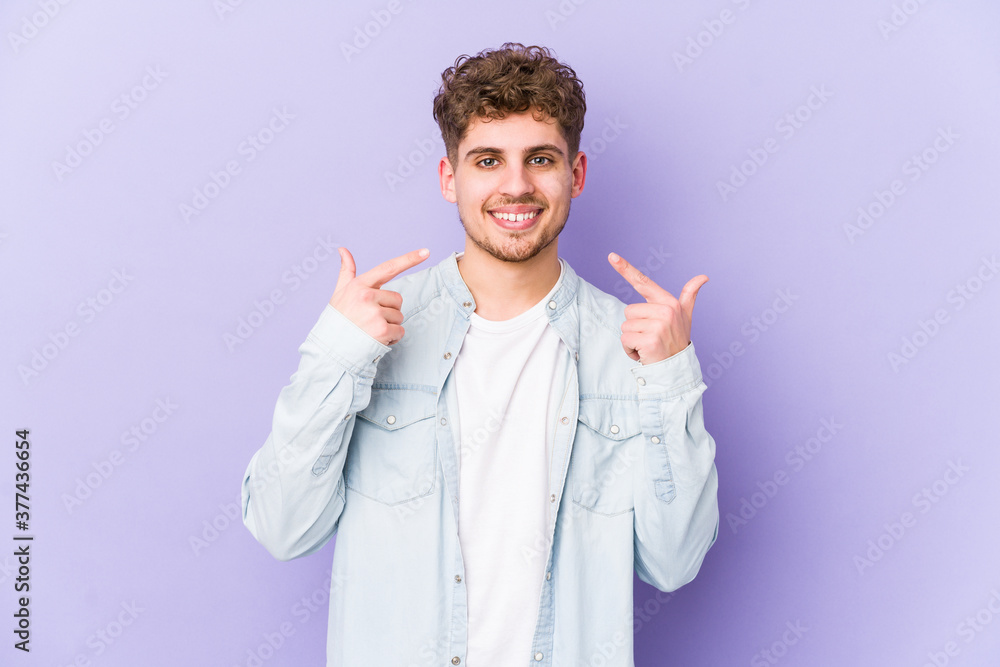Young blond curly hair caucasian man isolated smiles, pointing fingers at mouth. Young blond curly hair caucasian man isolated smiles, pointing fingers at mouth.