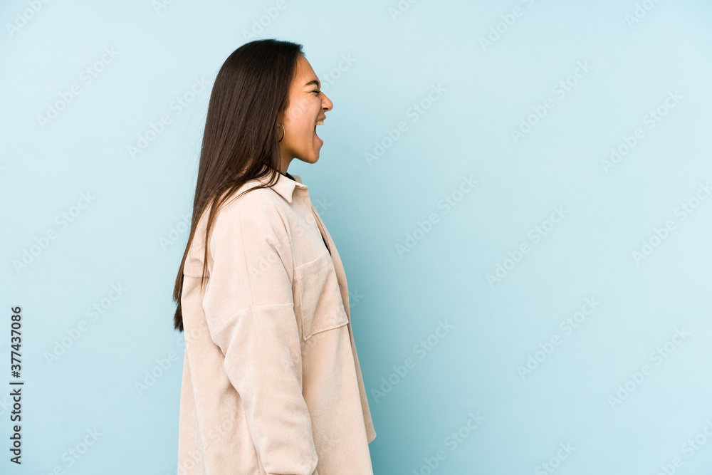 Young woman isolated on a blue background shouting towards a copy space Young woman isolated on a blue background shouting towards a copy space