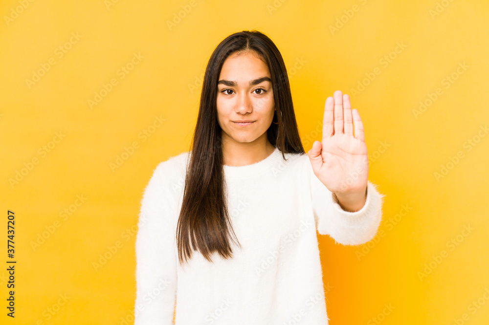 Young woman isolated on a yellow background standing with outstretched hand showing stop sign, preventing you. Young woman isolated on a yellow background standing with outstretched hand showing stop sign, preventing you.