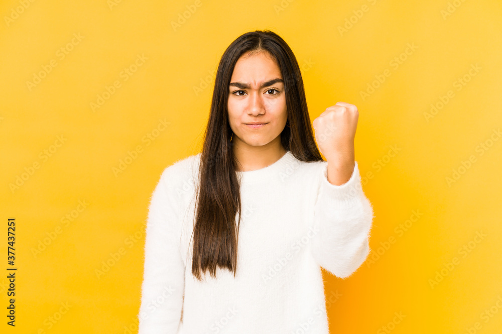 Young woman isolated on a yellow background showing fist to camera, aggressive facial expression. Young woman isolated on a yellow background showing fist to camera, aggressive facial expression.