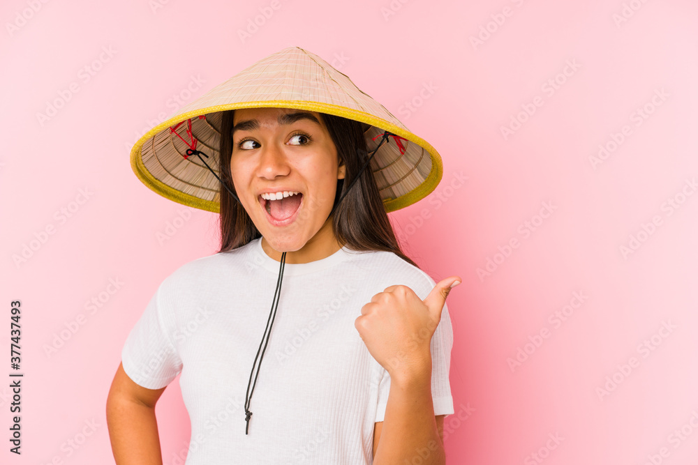 Young asian woman wearing a vietnamese hat isolated Young asian woman wearing a vietnamin hatpoints with thumb finger away, laughing and carefree. Young asian woman wearing a vietnamese hat isolated Young asian woman wearing a vietnamin hatpoints with thumb finger away, laughing and carefree.