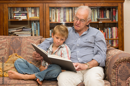 Grandfather and grandson reading a book on a sofa together photo
