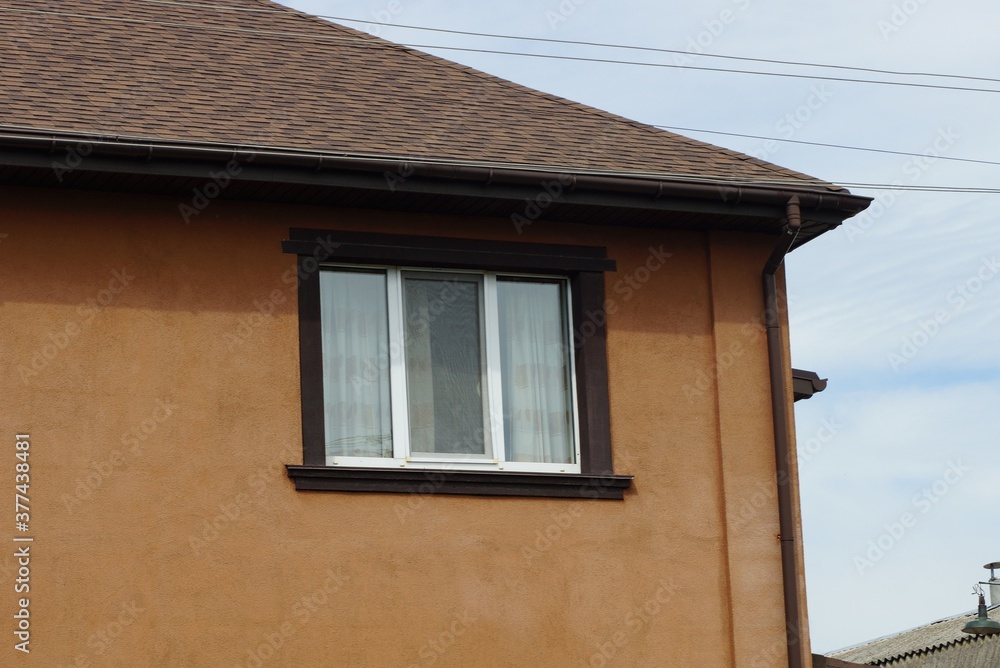one large window on a brown wall of a private house under a tiled roof against the sky one large window on a brown wall of a private house under a tiled roof against the sky