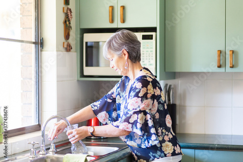 senior woman filling water jug from tap in kitchen