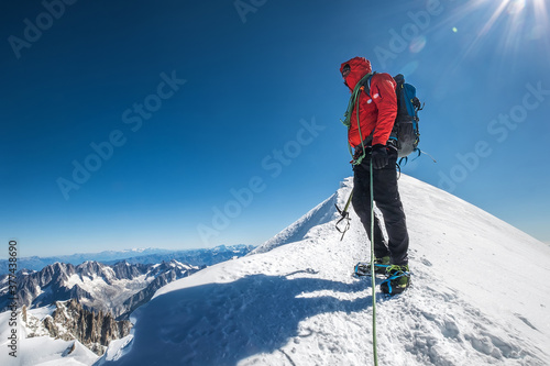 Last steps before Mont Blanc (Monte Bianco) summit 4,808 m of rope team man with climbing axe dressed mountaineering clothes, boots with crampons walking by snowy slopes with blue sky background