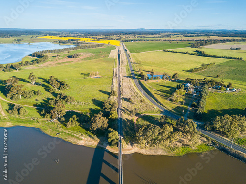 Aerial view of railway line and a country road converging as they cross a river