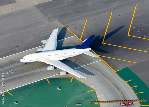 Aerial view of large white unidentified aircraft in an international airport runway before take off. Runway and taxiway signs. Airplane near yellow chevrons.