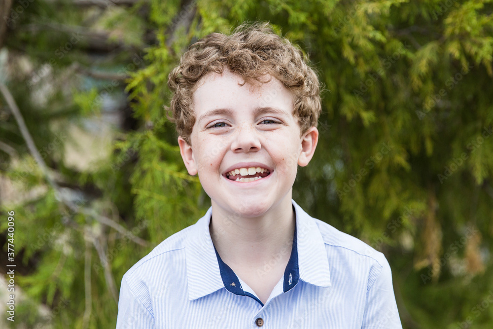 Young boy with curly hair standing in front of tree smiling Young boy with curly hair standing in front of tree smiling