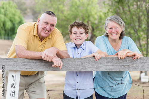 Retired husband and wife grandparents leaning on fence at home happy smiling with grandson