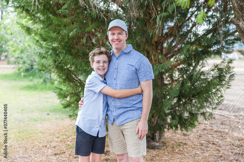 Father and son standing together under tree at home in yard smiling Father and son standing together under tree at home in yard smiling