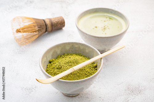 Matcha green tea powder with bamboo matcha whisk brush setup on white concrete background .