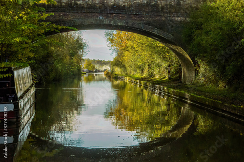 Autumn reflections of Wolfhamcote Bridge No 98, narrowboats, autumn leaves, colors, Oxford Canal near Wolverton, England. Peaceful autumn light. Picturesque, scenic. Canal life. Destination holiday.