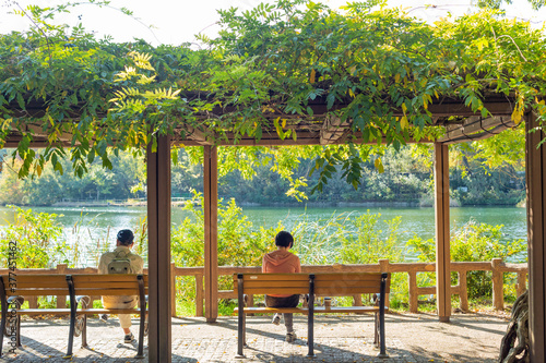 two persons sitting on a bench in front of lake in inokashira park, tokyo, japan photo