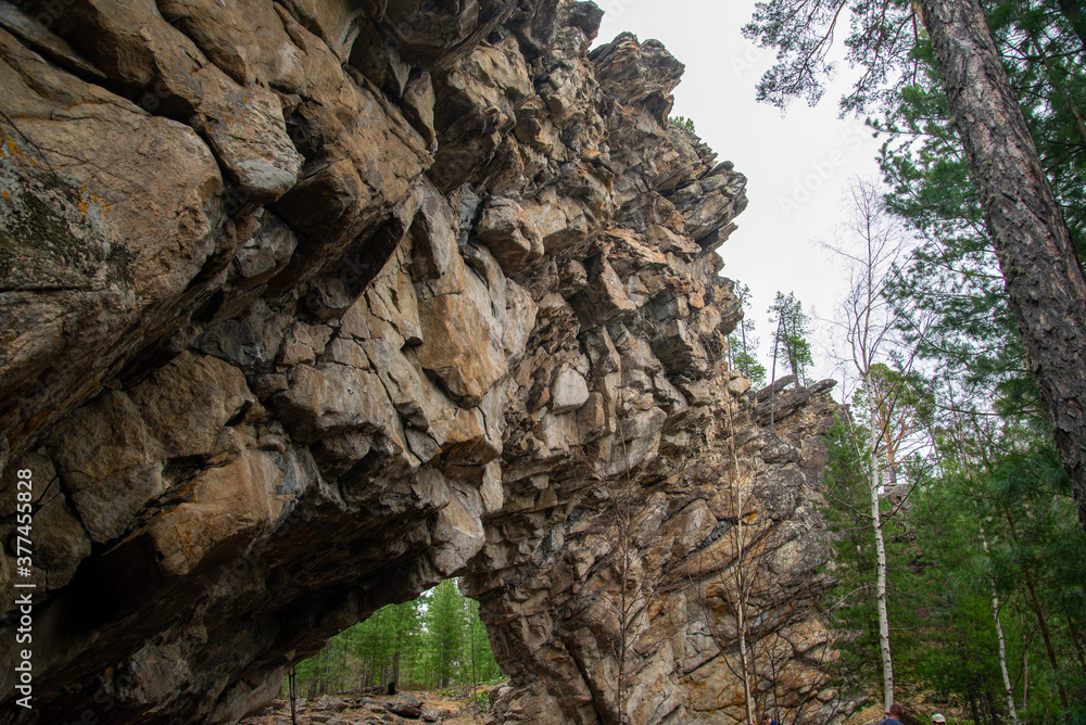 
Stone mountains. 
Stone texture. Mountain gorge. Among the huge rocky mountains there is a mountain river, the mountains are covered with fresh bright green foliage of trees in early spring.
