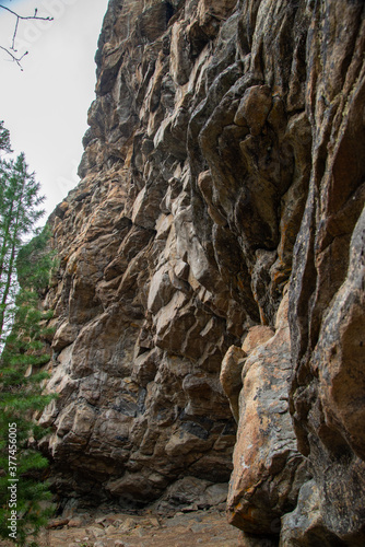  Stone mountains. Stone texture. Mountain gorge. Among the huge rocky mountains there is a mountain river, the mountains are covered with fresh bright green foliage of trees in early spring. 