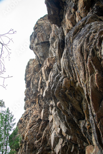 
Stone mountains. 
Stone texture. Mountain gorge. Among the huge rocky mountains there is a mountain river, the mountains are covered with fresh bright green foliage of trees in early spring.
