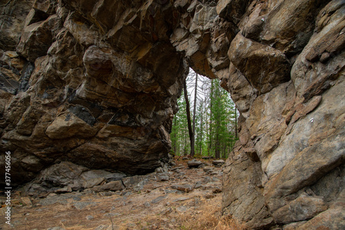 
Stone mountains. 
Stone texture. Mountain gorge. Among the huge rocky mountains there is a mountain river, the mountains are covered with fresh bright green foliage of trees in early spring.

