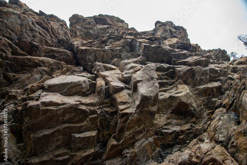 
Stone mountains. 
Stone texture. Mountain gorge. Among the huge rocky mountains there is a mountain river, the mountains are covered with fresh bright green foliage of trees in early spring.
