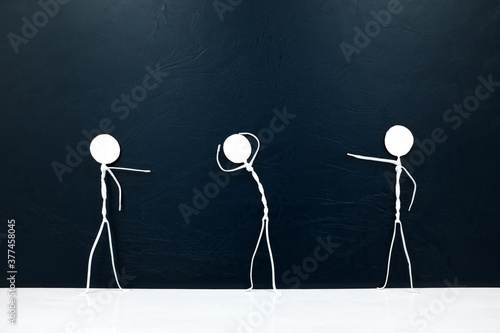People figures pointing fingers on a scared stick man  on a dark background. Bullying, victim blaming, accusation and abuse concept. photo