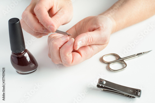 Woman doing manicure to herself. Female hands  holding nail file  with nail polish  scissors and nail clippers on white background.