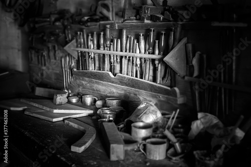 Black and white scene of an old wood working bench. There are chisels, wood, and other tools sitting on top of the bench. © Scott Book