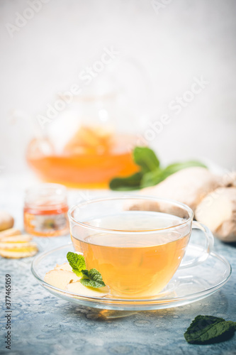 Ginger tea in a glass cup with lemon and mint on light background