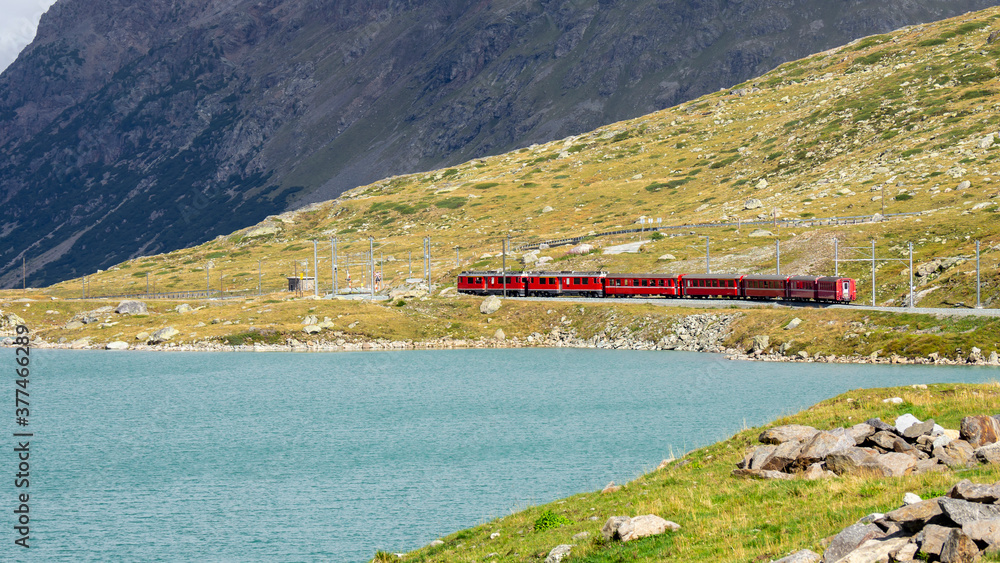 Bernina mountain pass. The famous red train is crossing the white lake. Amazing landscape of the Switzerland land. Best of Swiss. Famous destination and tourists attraction