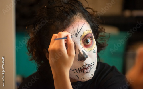 Mujer mexicana latina maquillando cara catrina calavera día de muertos tradición luz tenue, acercamiento, detalle, cuidadosa perfeccionista photo