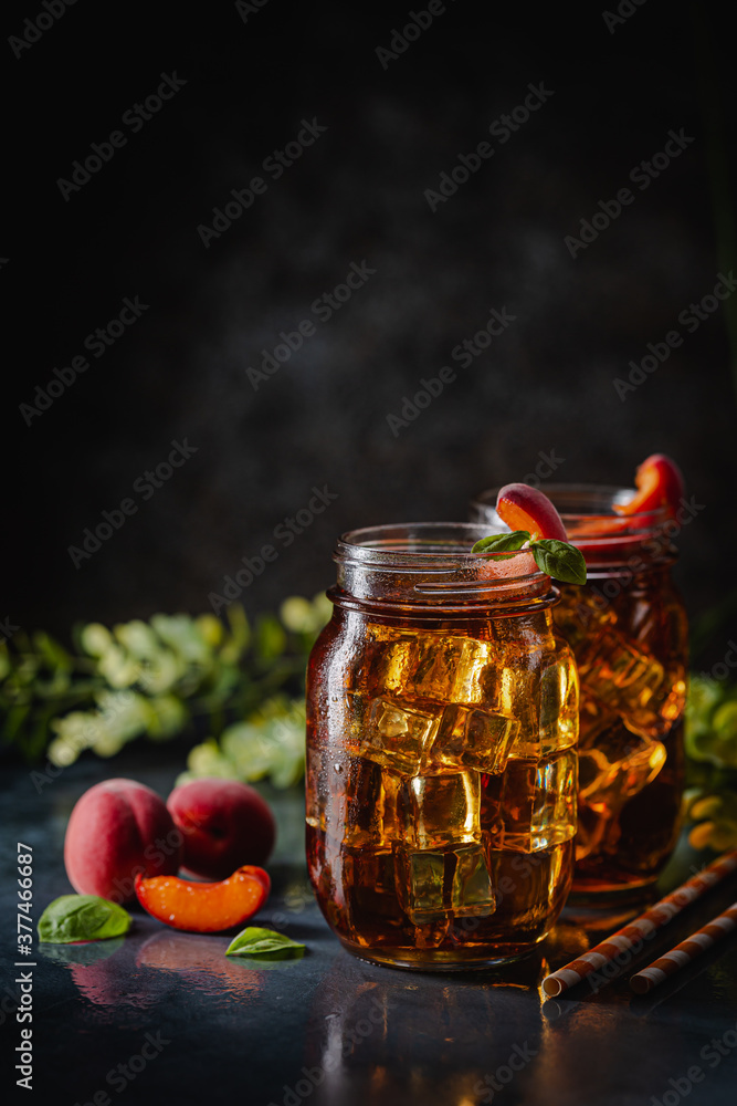 Glass of peach or apricot iced tea with fruit slices against dark blue background Glass of peach or apricot iced tea with fruit slices against dark blue background