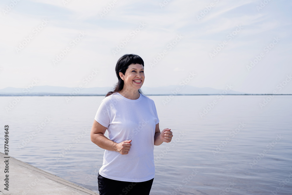 Active laughing senior woman jogging near the riverside