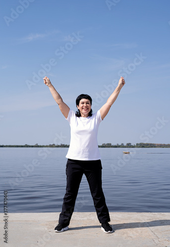 Active and happy senior woman exercising near the riverside