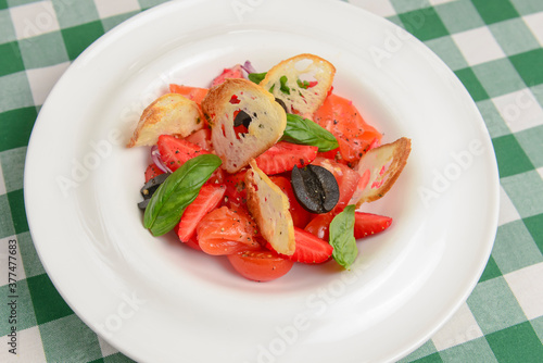 Summer salmon salad with strawberry, tomato, olives and basil in a white plate. Traditional Italian cuisine concept.