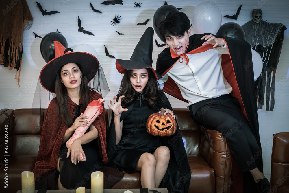 Obraz premium Young happy Asian people dressing Halloween costume, vampire and witch, celebrating in party. Holding fake arm and hand. Looking at camera.
