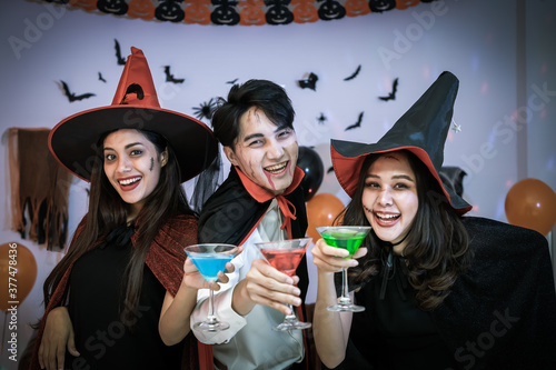 Young happy Asian people dressing Halloween costume, vampire and witch, celebrating in party. Holding and clinking wine glass. Looking at camera.