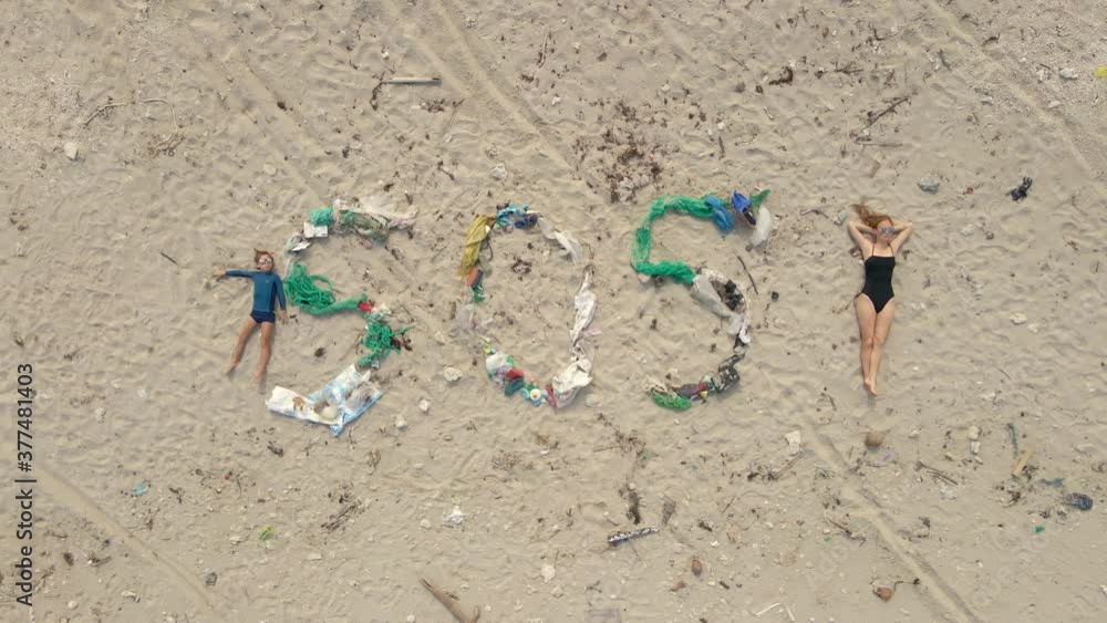 Aerial shot of the song SOS made of trash on a beach. A woman and a boy lay by the sign. Ecological disaster concept. Plastic pollution concept Aerial shot of the song SOS made of trash on a beach. A woman and a boy lay by the sign. Ecological disaster concept. Plastic pollution concept