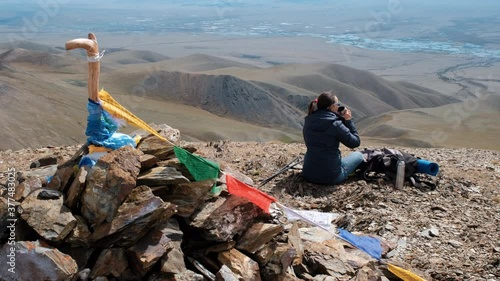 Female Sitting on the Rock and Drinking Hot Tea. She is Enjoying Amazing Scenery from the Top of a Mountain. Colorful Buddhist Prayer Flags Waving in the Wind on the Foreground. Slow Motion.