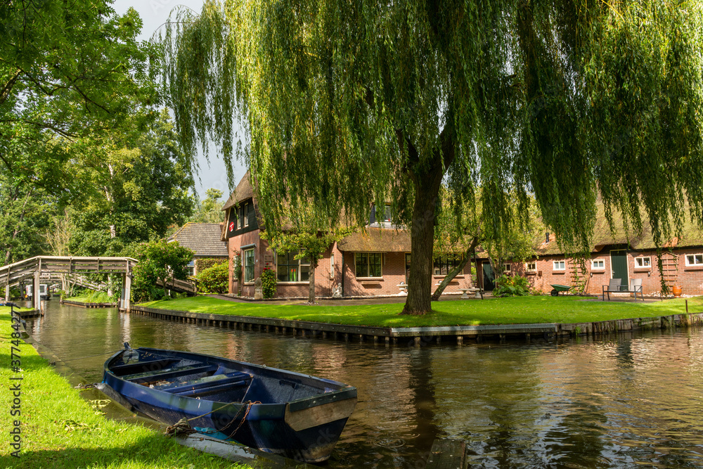 Weeping willow and boat in front of a traditional Dutch house in Giethoorn