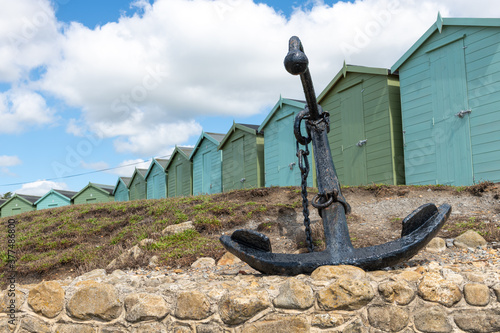 Photo of the anchor at Charmouth beach with beach huts in the background photo