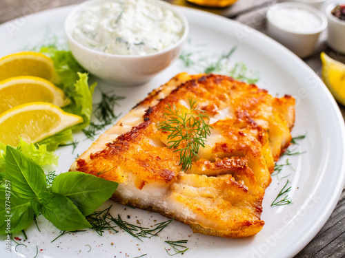 Fish dish - fried cod fillet with cream sauce and lemon served on wooden table
