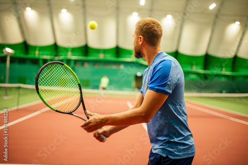 Instructor or coach teaching how to play tennis on a court indoor © yurakrasil