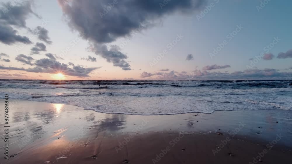 The waves of the sea smoothly spread along the sandy shore at sunset. Sunset at the sea. The waves of the sea smoothly spread along the sandy shore at sunset. Sunset at the sea.